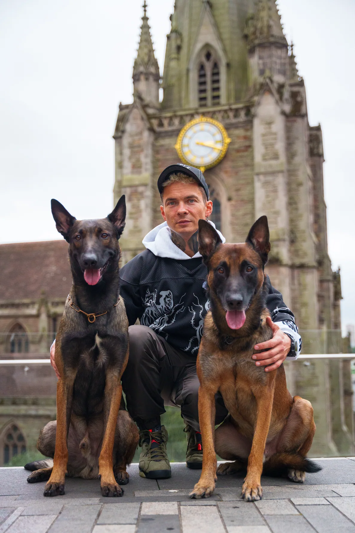Andrejus and his two working dogs posing in front of a clock tower