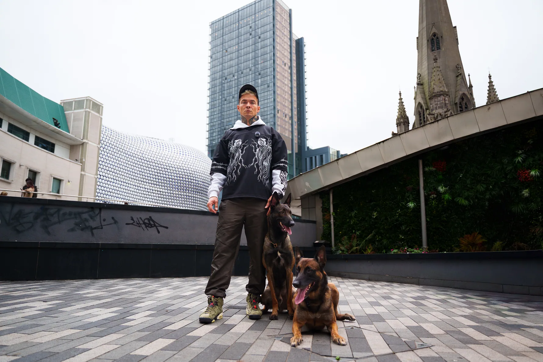 Andrejus practising obedience with two dogs beside Birmingham landmarks